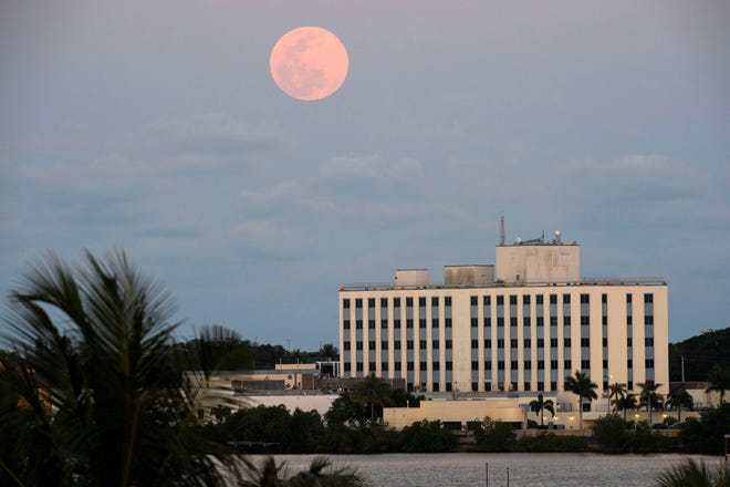 As the sun sets over the St. Lucie River, April's full moon, the brightest supermoon of the year, rises in the east over Cleveland Clinic Martin North Hospital on Tuesday, April 7, 2020, in Stuart, Fla.