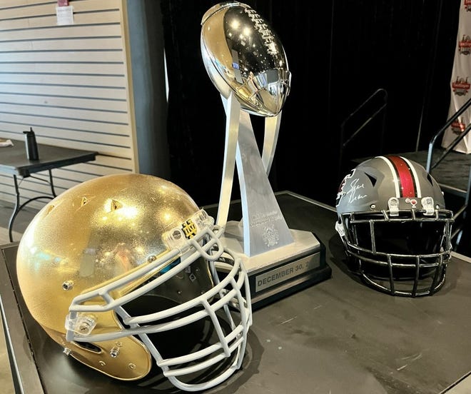 The helmets of Notre Dame (left) and South Carolina (right) flank the Ash Verlander Trophy for the winner of Friday's TaxSlayer Gator Bowl.