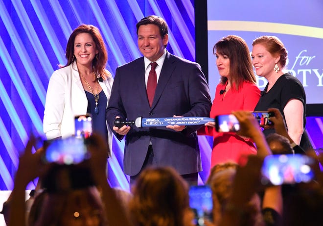 Florida Governor Ron Desantis, center, is presented "The Sword of Liberty" by Moms for Liberty co-founders Tiffany Justice, left, Tina Descovich, second from right and executive director of program outreach Marie Rogerson, far right, during the first Moms for Liberty National Summit on Thursday, July 15, 2022 in Tampa, Fla.