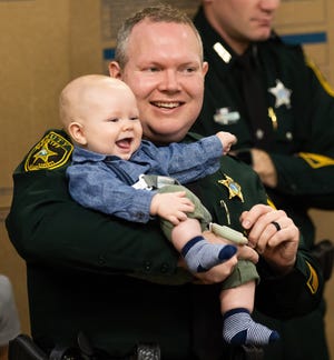 Marion County Sheriff's Chaplain Vernon Phillips holds his 6-month-old son, Gunner, at Gov. Ron DeSantis' press conference on Wednesday.