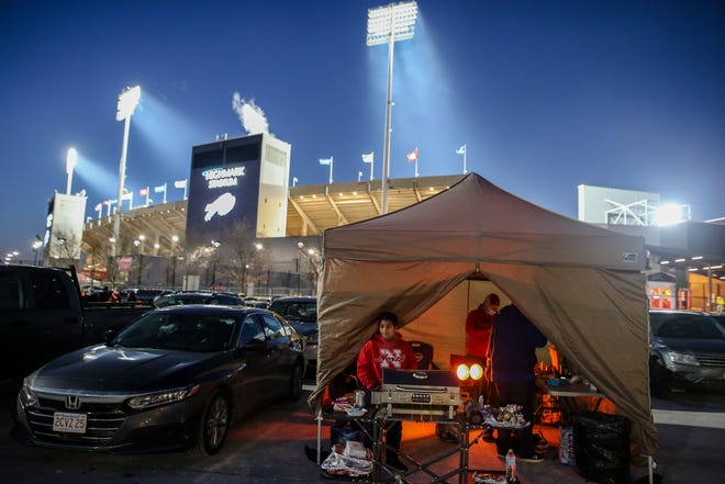 The Ammons and McFadden families tailgate inside a tent as temperatures drop in the parking lots outside of Highmark Stadium before an NFL wild-card playoff football game between the Buffalo Bills and the New England Patriots, Saturday, Jan. 15, 2022, in Orchard Park, N.Y. (AP Photo/Joshua Bessex)