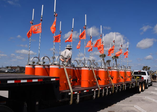 A truckload of mystery aquatic items are sitting on a tractor trailer bed in the parking lot of Patrick Space Force Base. The bright orange objects are numbered, have antenna and each one has two boat propellers protruding from them.