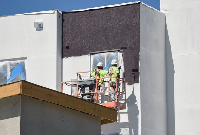 Construction workers paint around a 4th floor window outside of the phase 1 buildings on the Blue Sky Landing apartment complex on Monday Feb. 13, 2023, in Fort Pierce. When completed Blue Sky Landing will have four buildings overlooking a pond, along with with a fitness center and a swimming pool.