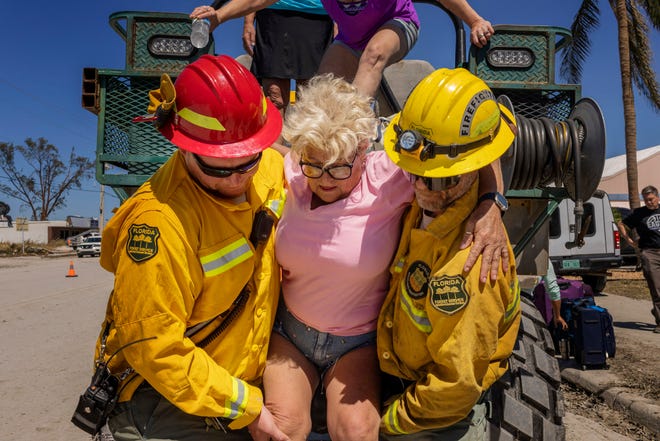 Diana Kauth is helped off a rescue rig by Florida Forest Service firefighters after riding out Hurricane Ian inside her neighbor’s two-story home in Fort Myers Beach, on San Carlos Island, on Friday, Sept. 30, 2022.