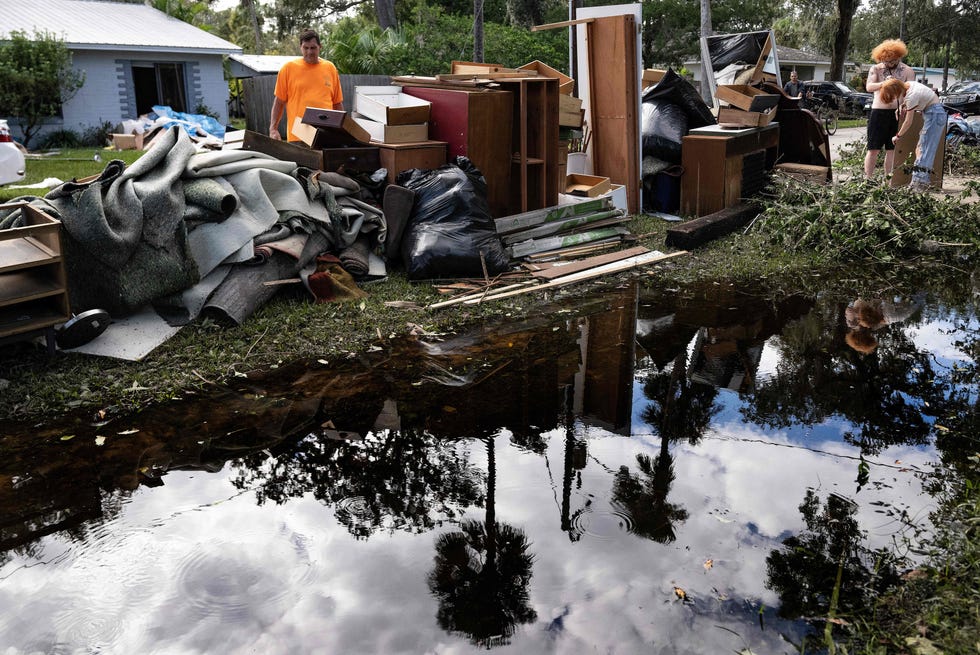 Michael Luff' stacks items from her flooded home on the curb in the aftermath of Hurricane Ian in New Smyrna Beach, Florida, on Oct. 3, 2022. - The confirmed death toll from Hurricane Ian, which slammed the southeast United States last week, has risen to at least 62, officials said on Oct. 2, 2022.