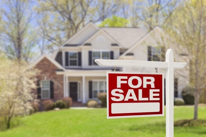 A For Sale sign in front of a two-story house surrounded by trees and a lawn.