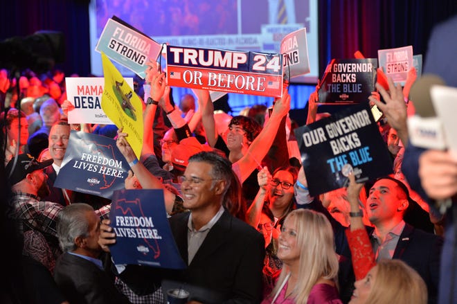 Supporters of Florida Gov. Ron DeSantis cheer and wave banners in the background of a live TV broadcast  Tuesday night, Nov. 8, 2022, during DeSantis' election night watch party at the  Tampa Convention Center.