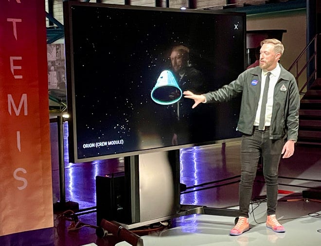 NASA TV commentator Dan Huot gestures at an artist's rendering of an Orion crew module during a live broadcast Tuesday night from the Kennedy Space Center Visitor Complex.