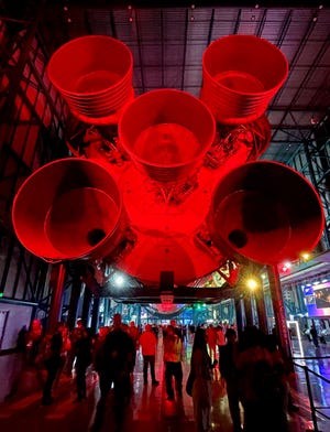 Artemis I launch spectators stroll beneath a 363-foot Saturn V moon rocket Tuesday night at the Kennedy Space Center Visitor Complex.