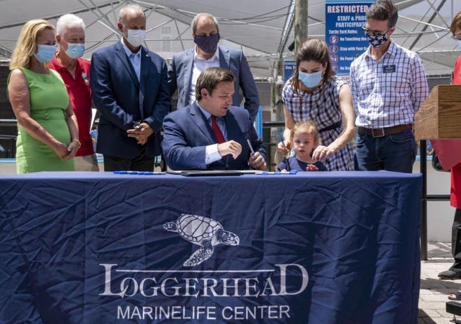 Gov. Ron DeSantis, center, asks his daughter Madison with first lady Casey DeSantis, to hand out markers for the signing of two bills related to protecting the state's environment at the Loggerhead Marinelife Center in Juno Beach.