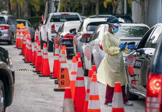 A health care worker gets information from peopled lined up to be tested at a COVID-19 testing site outside the Gardens Branch Library in Palm Beach Gardens, Florida on December 20, 2021. The tests were covered by Medicare and Medicaid for policyholders.