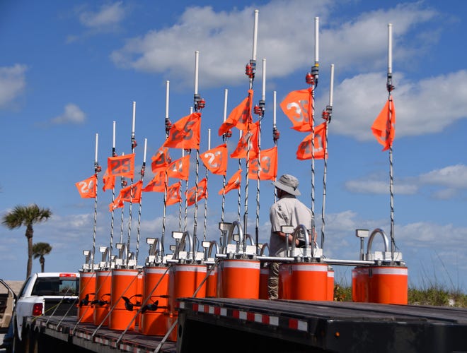 A truckload of mystery aquatic items are sitting on a tractor trailer bed in the parking lot of Patrick Space Force Base. The bright orange objects are numbered, have antenna and each one has two boat propellers protruding from them.