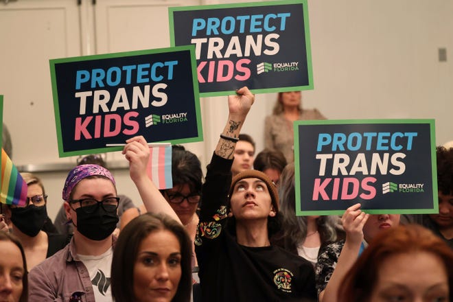 People hold signs during a joint board meeting of the Florida Board of Medicine and the Florida Board of Osteopathic Medicine last year in Lake Buena Vista, Fla., to establish new guidelines limiting gender-affirming care in Florida.