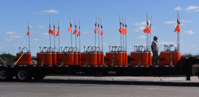 A truckload of mystery aquatic items are sitting on a tractor trailer bed in the parking lot of Patrick Space Force Base. The bright orange objects are numbered, have antenna and each one has two boat propellers protruding from them.